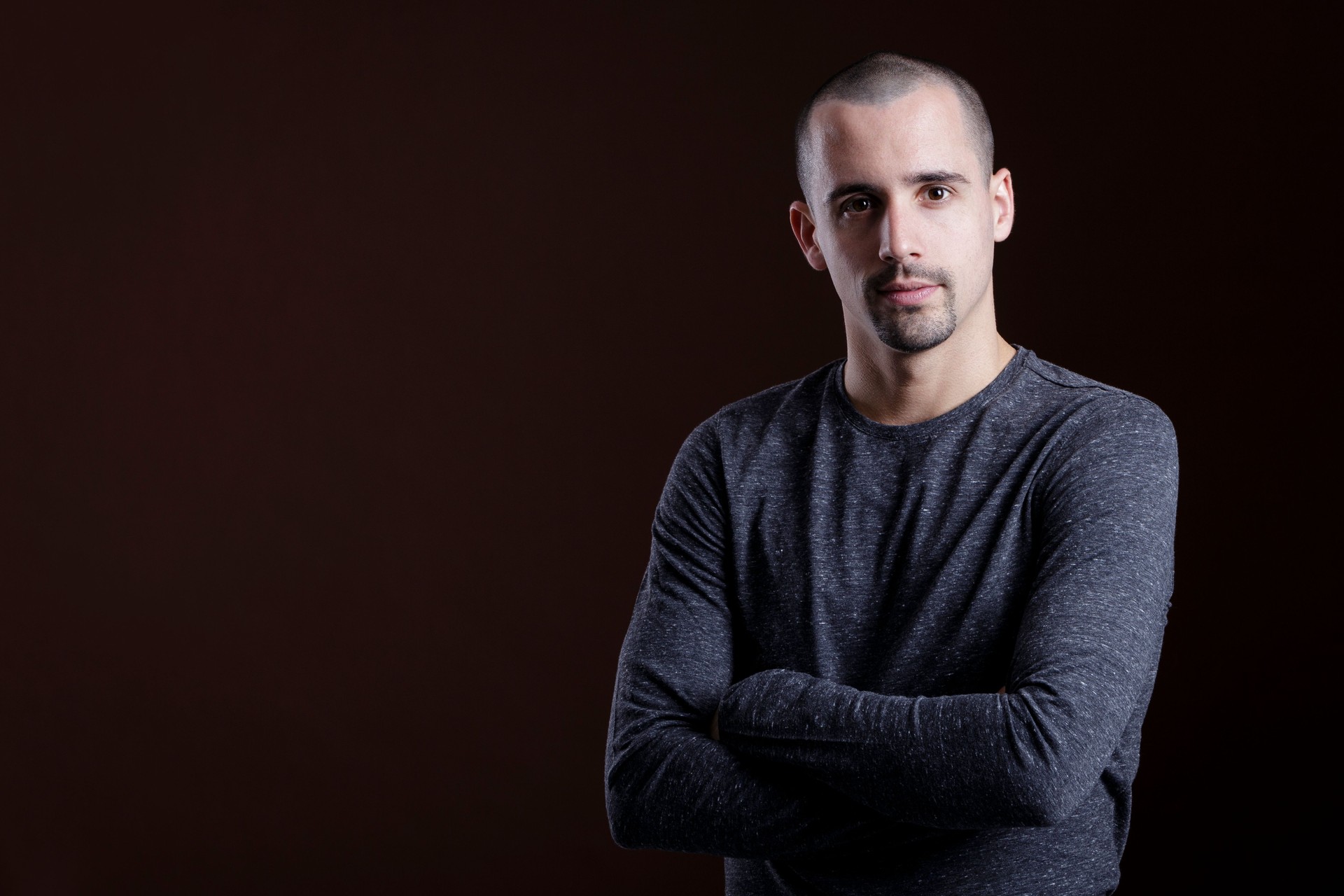 Portrait Of Young Man With Arms Crossed Against Brown Background