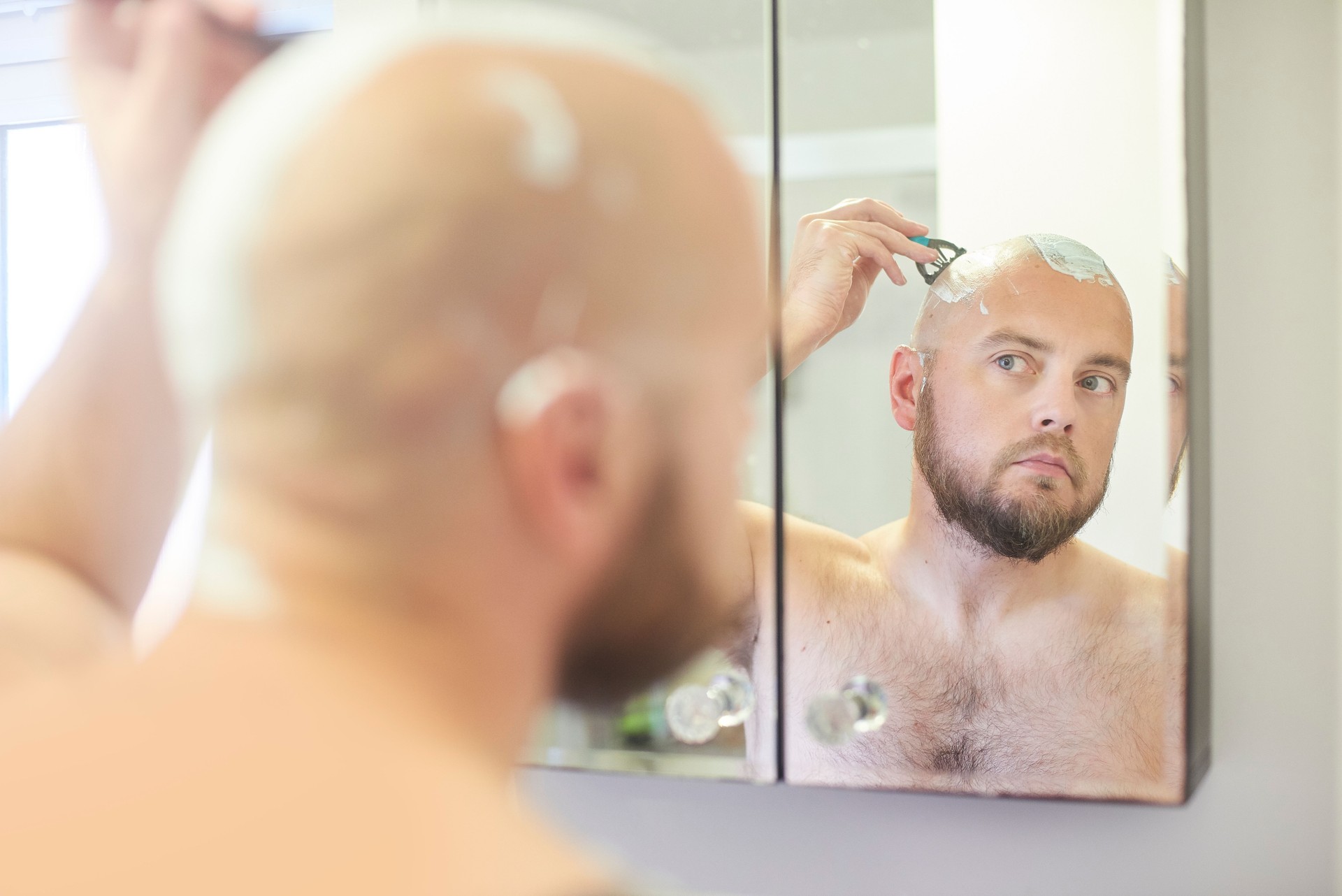 Male shaving head in the bathroom